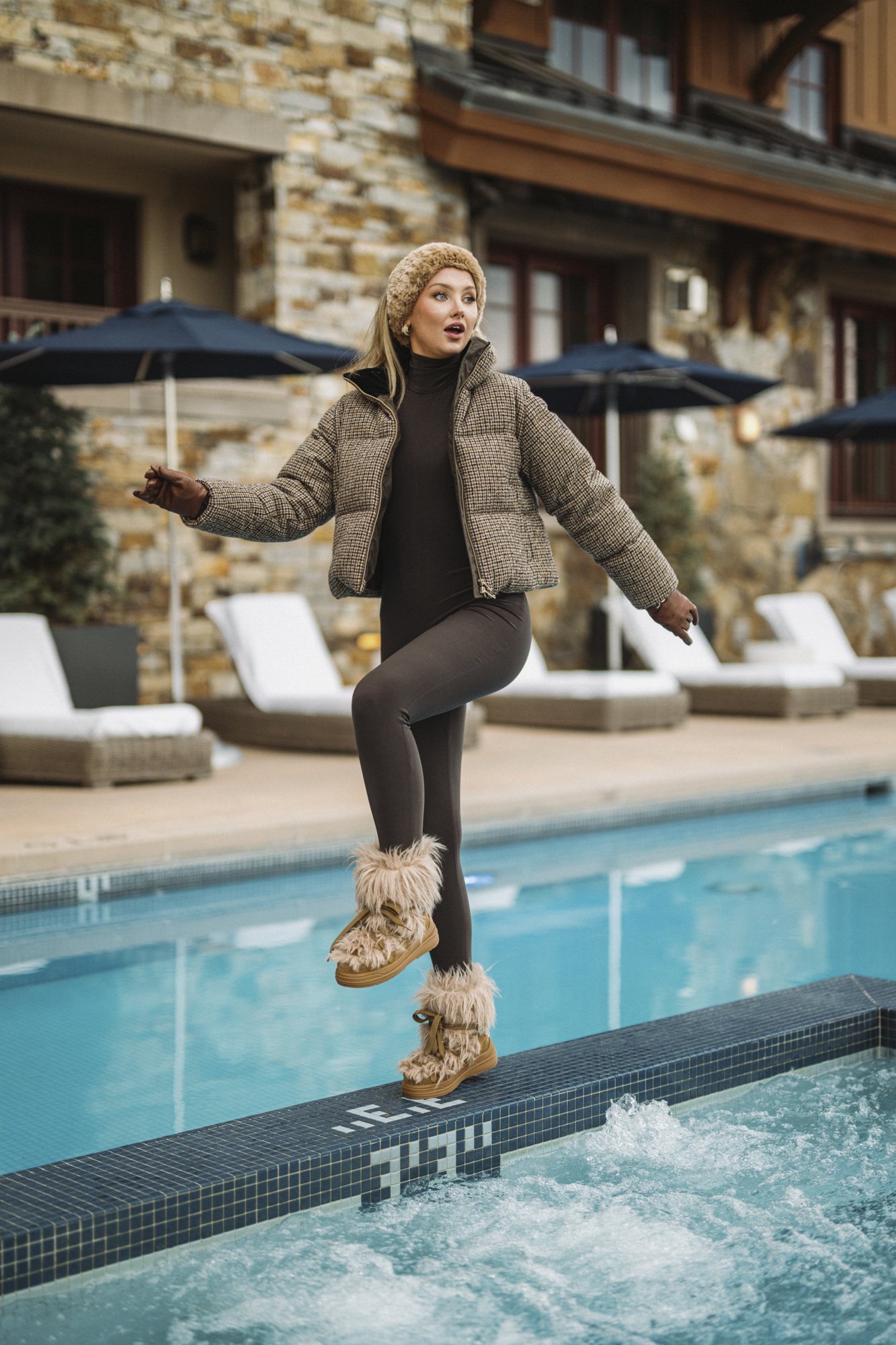 Kicking up a leg at the edge of a resort pool in a houndstooth puffer, leggings and fur boots