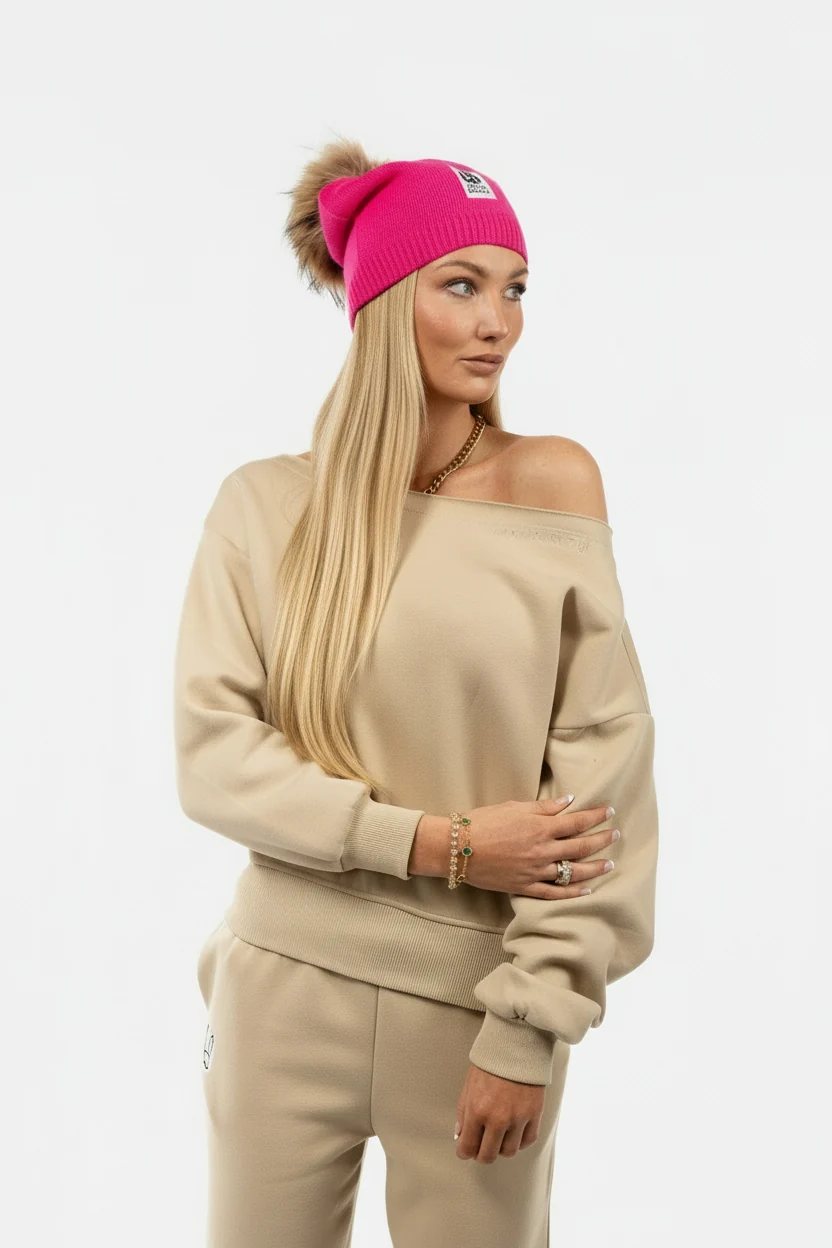 Studio portrait in a tan off-shoulder sweatshirt and pink beanie with a fur pom