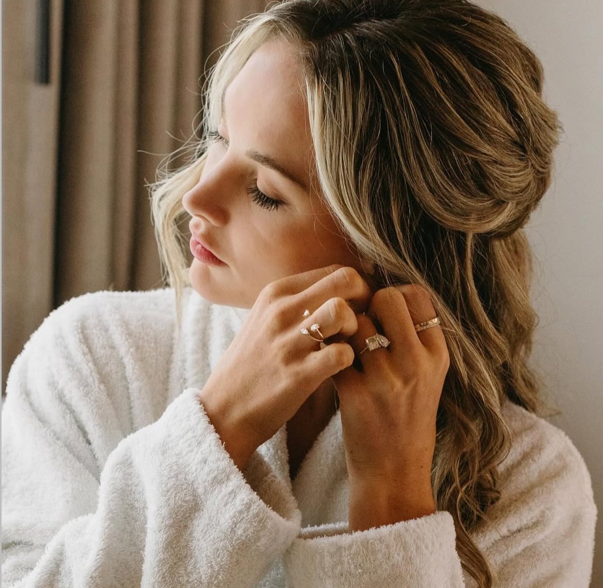 Close portrait in a white robe putting on rings and earrings, hair half up