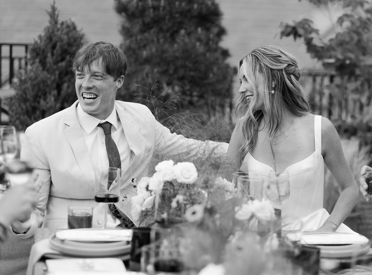 Black and white image of the bride and groom laughing at the reception table