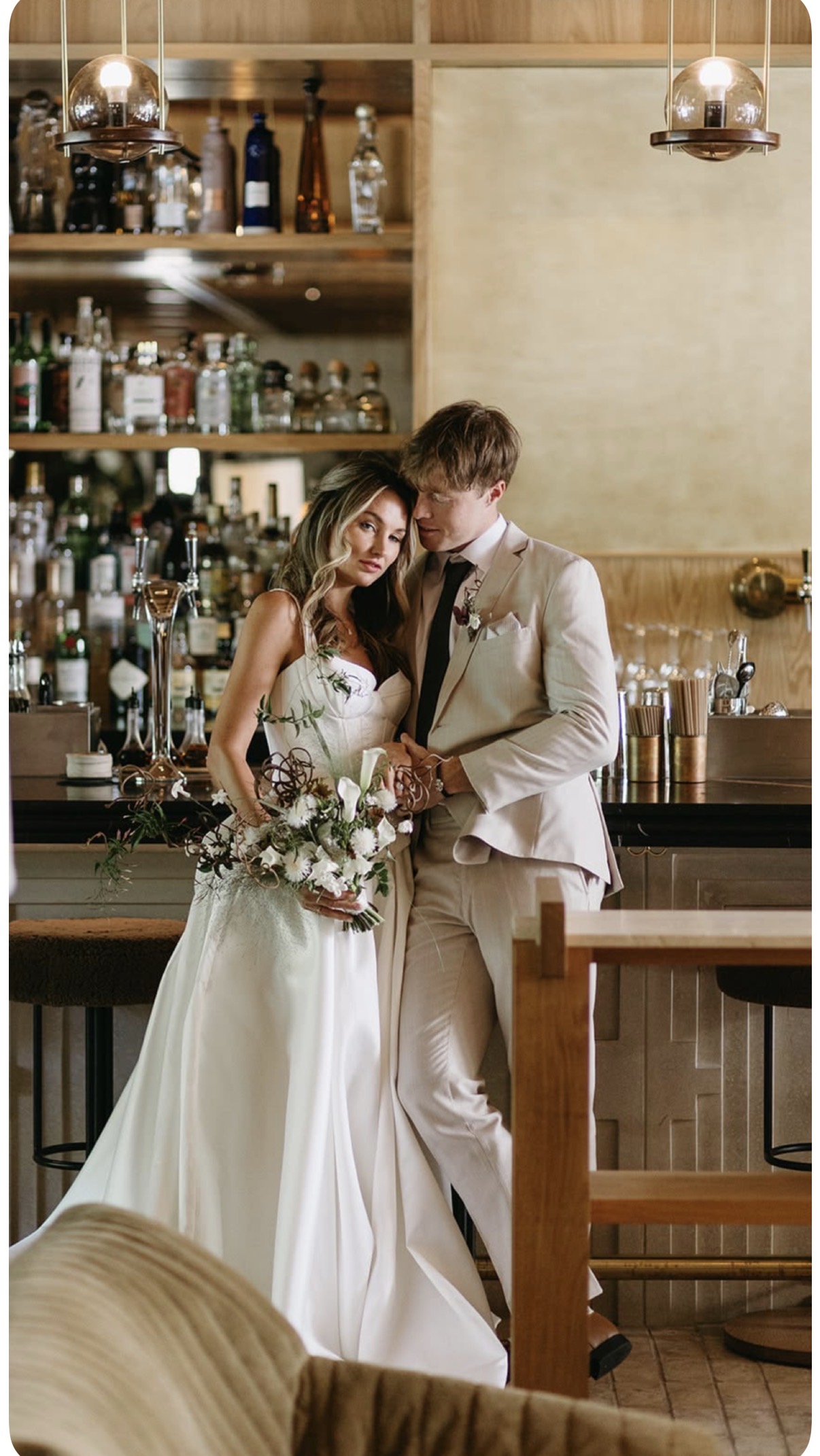 Bride and groom leaning together against a bar, bride holding a white bouquet