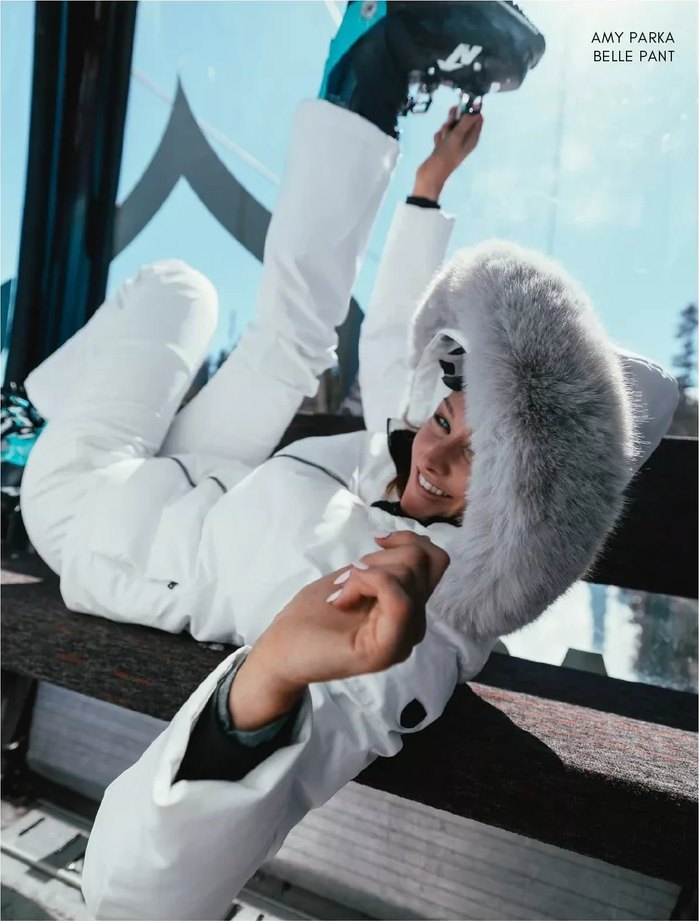 Smiling in a white ski suit and fur-trimmed hood, laughing on a gondola seat